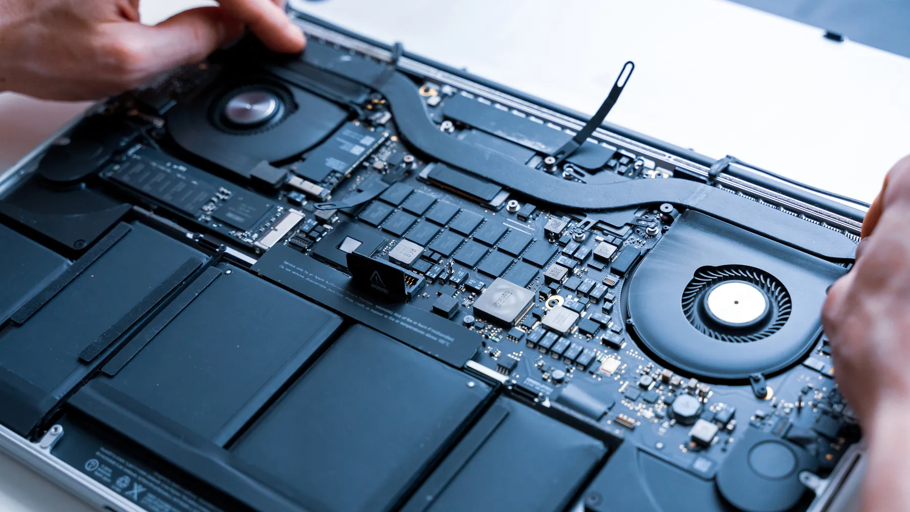 A technician's hands opening a MacBook to repair it.